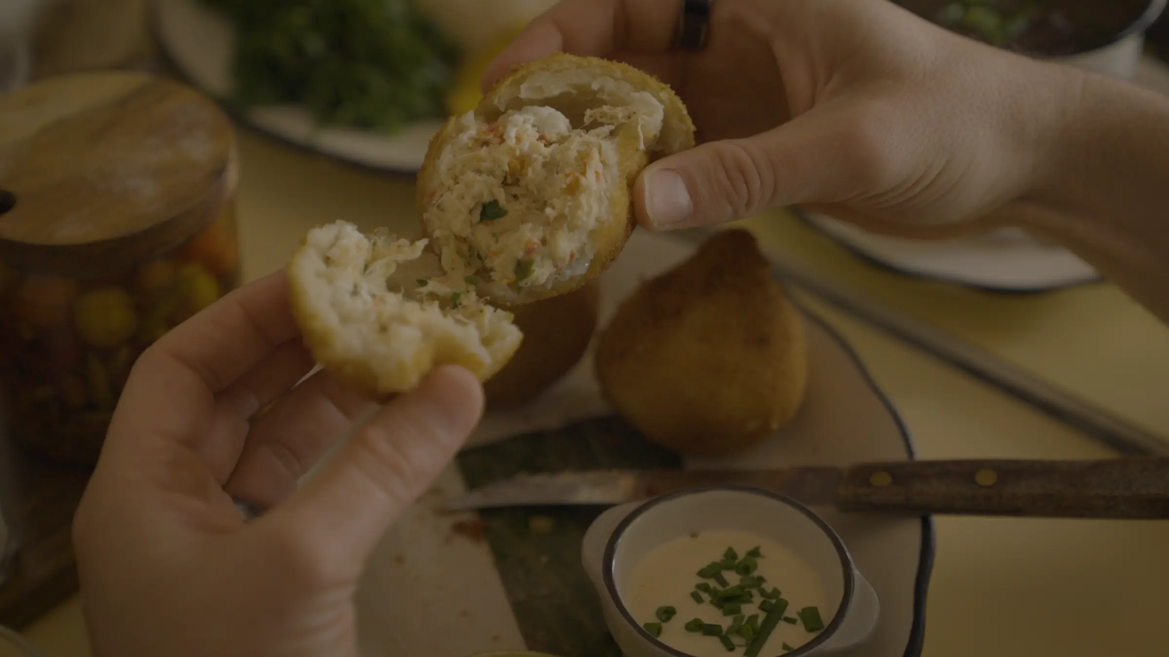 Hands breaking open a freshly fried stuffed pastry at the table